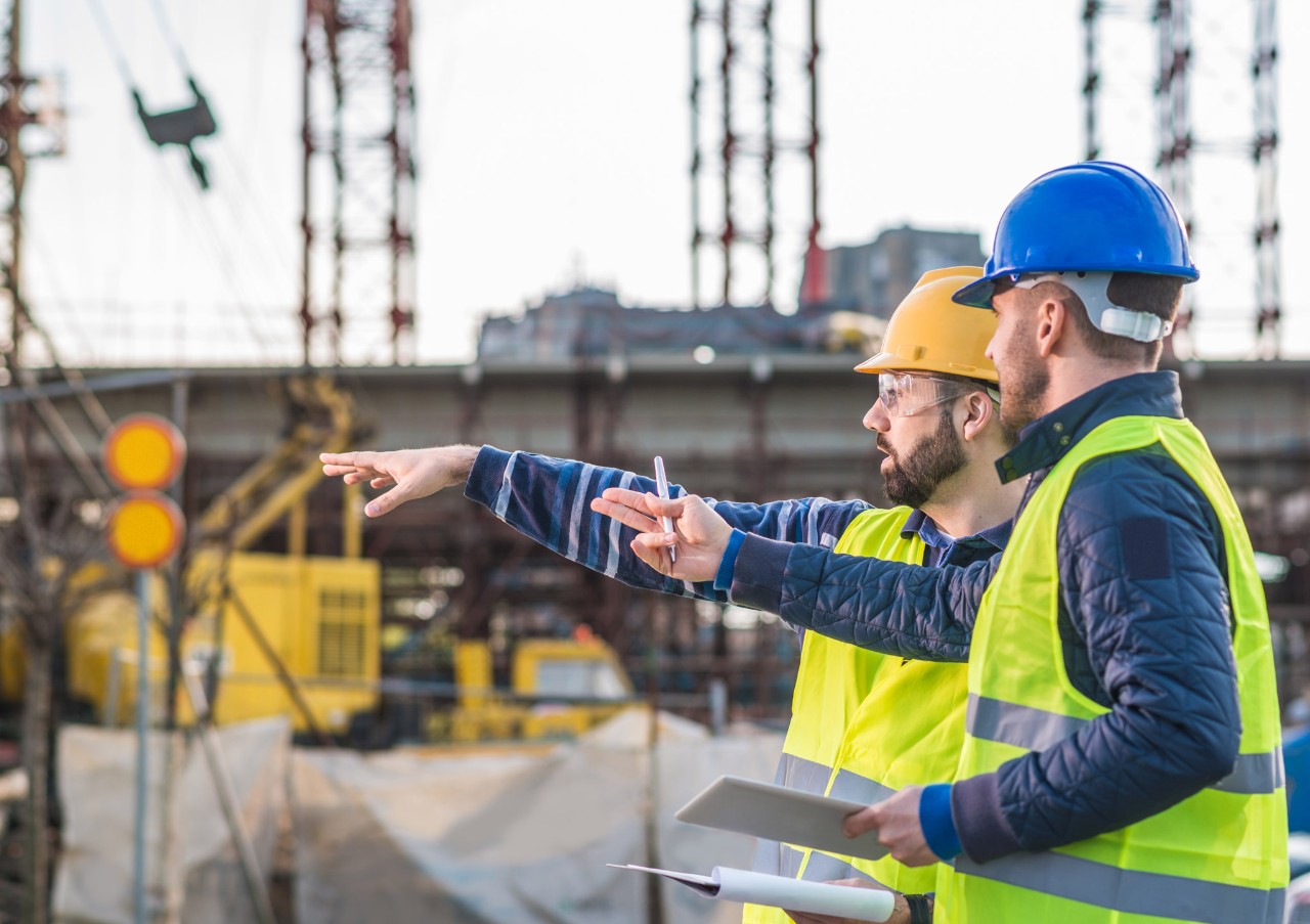 Engineers and contractors on construction site, following the progess of bridge and road infrastructure development. Two experts on construction platform in reflective wear with hardhats discussing project phases and successful previous developments. Image taken with Nikon D800 and 85mm lens, developed from RAW in XXXL size. Location: Central Europe, Europe